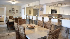 A modern kitchen with white cabinets, a stainless steel microwave, and a dining area with wicker chairs and a marble table. - The Seascape Premier Beachfront Cottage: Gulf View, Pool, Hot Tub, BBQ, WiFi (Indian Shores)