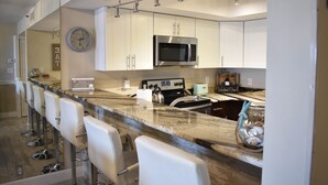 A modern kitchen with white cabinets, a stainless steel microwave, a built-in oven, and a marble countertop. - The Seascape Premier Beachfront Cottage: Gulf View, Pool, Hot Tub, BBQ, WiFi (Indian Shores)