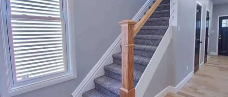 Una escalera con barandillas de madera y alfombra estampada, que conduce a una puerta oscura.