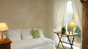 Une chambre à coucher avec un lit, deux lampes de chevet, une petite table sur laquelle est posé un vase de fleurs, et une fenêtre avec des rideaux.