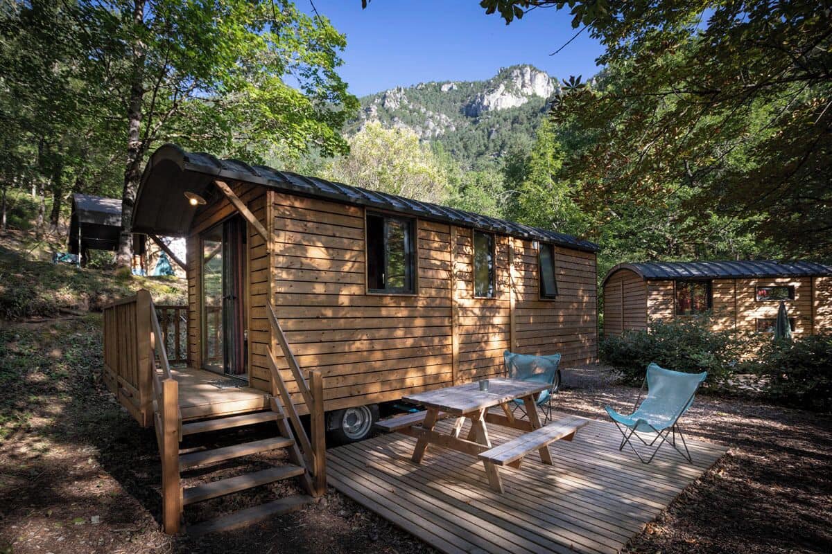 A wooden cabin with a deck, a small table, and two chairs.