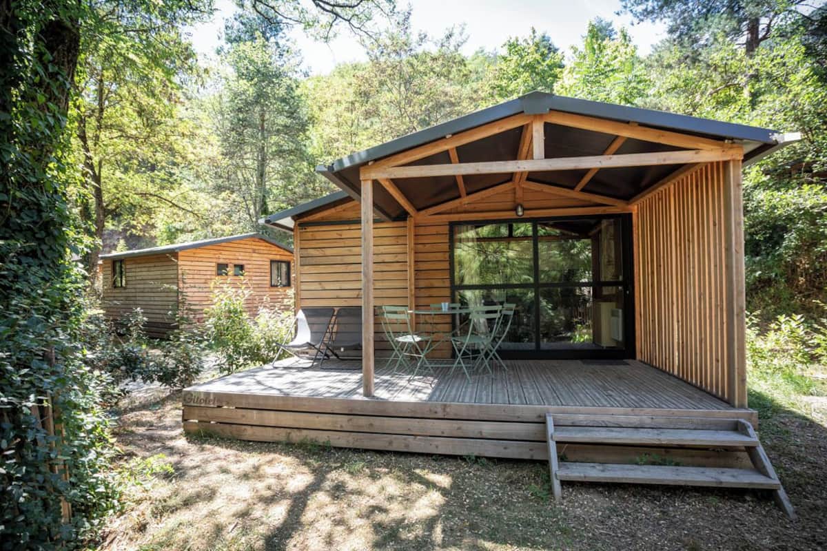 A wooden cabin with a deck and outdoor seating area, surrounded by trees.