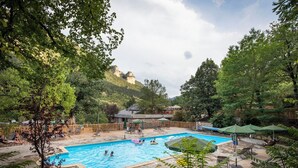 Uma piscina rodeada por espreguiçadeiras e guarda-sóis, com vista para uma colina arborizada ao fundo.