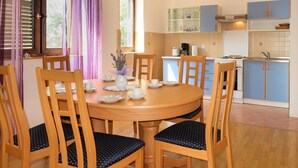 Un comedor con una mesa redonda de madera, seis sillas de madera con asientos acolchados y una ventana con cortinas moradas.