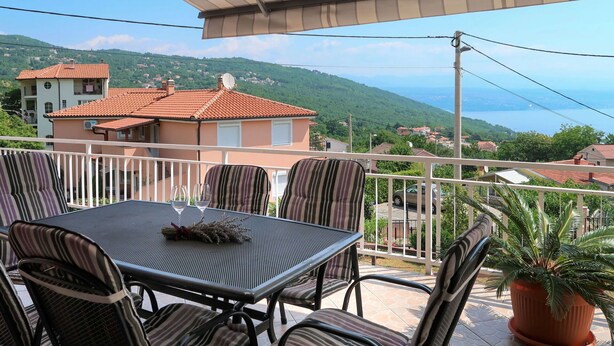 Un balcón con una mesa y sillas, una planta en maceta y vistas a una colina con casas.