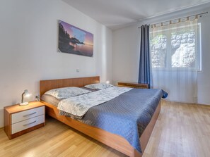 Ein Schlafzimmer mit einem hölzernen Bett, einem Nachttisch mit Lampe, einem Wandbild und einem Fenster mit Vorhängen.