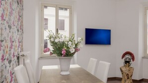 En matplats med ett vitt bord och stolar, en vas med blommor, en tv på väggen och en dekorativ staty.