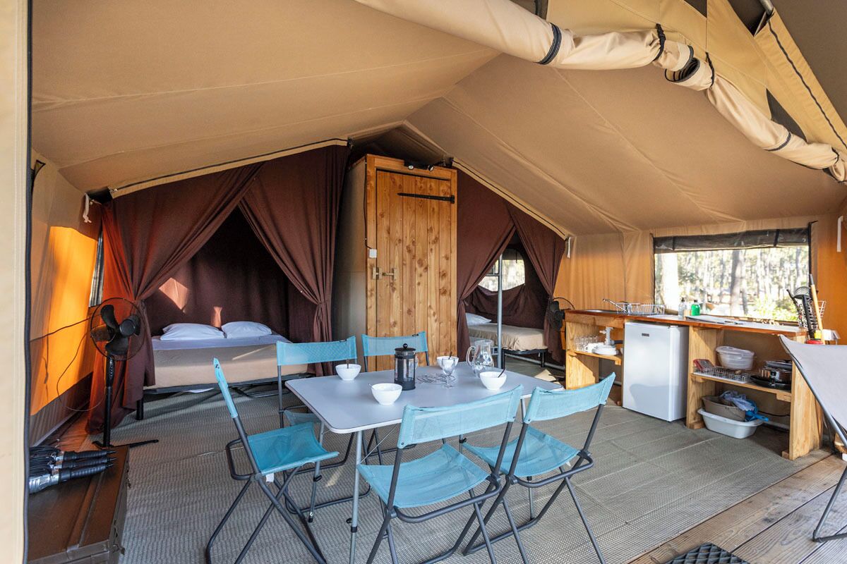 A compact, well-lit tent with a kitchenette, a dining area with foldable chairs, and a bed with curtains.