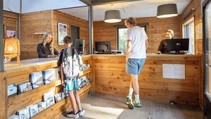 A wooden cabin with a reception desk, shelves with books, and a computer. - Huttopia Lac de Carcans (Carcans)
