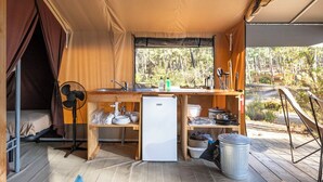 A compact kitchen with a refrigerator, sink, and fan, overlooking a forested area. - Huttopia Lac de Carcans (Carcans)