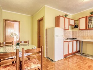 A compact kitchen with a refrigerator, wooden cabinets, a dining table with chairs, and a tiled backsplash. - Lovely apartment for 4 guests with A/C, WIFI, TV, patio and pets allowed (Crikvenica)