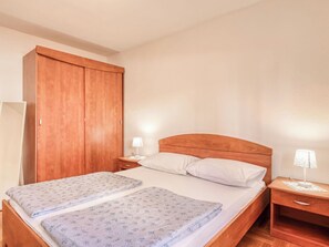 Een tweepersoonsbed met een houten hoofdbord, twee nachtkastjes met lampen en een ruime garderobekast.