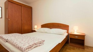 Een net opgemaakt bed met een bloemenprint deken, twee bedlampjes en een houten garderobe.