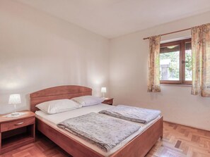 A bedroom with a wooden bed, two bedside tables, a window with curtains, and a wooden floor. - Lovely apartment for 4 guests with A/C, WIFI, TV, patio and pets allowed (Crikvenica)