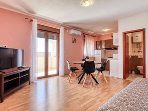 A living room with a television, a dining area with a table and chairs, and a kitchen with a sink and stove. - Lovely apartment for 4 people with A/C, WIFI, TV, patio and pets allowed (Crikvenica)