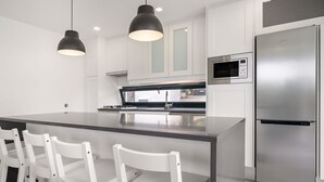 Una cocina moderna con una isla central, sillas blancas, un refrigerador de acero inoxidable e iluminación colgante.