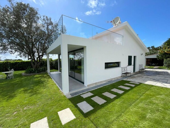 A modern house with a glass door entrance, a stone pathway, and a well-maintained lawn.