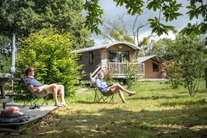 Two people relaxing in lawn chairs in a grassy area with a wooden deck and a small house in the background.