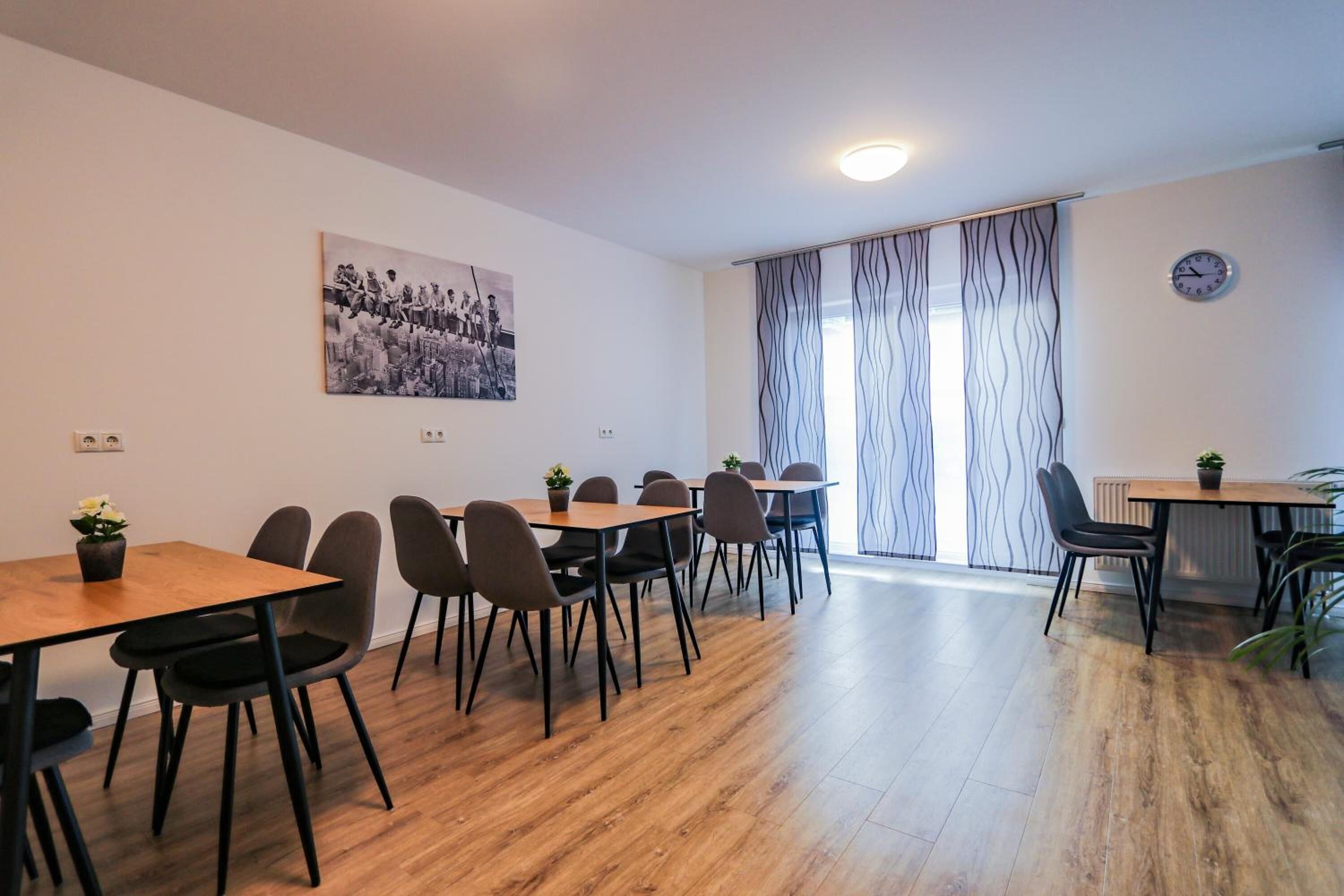 Un comedor moderno con mesas y sillas de madera, una fotografía blanco y negro en la pared y un reloj.
