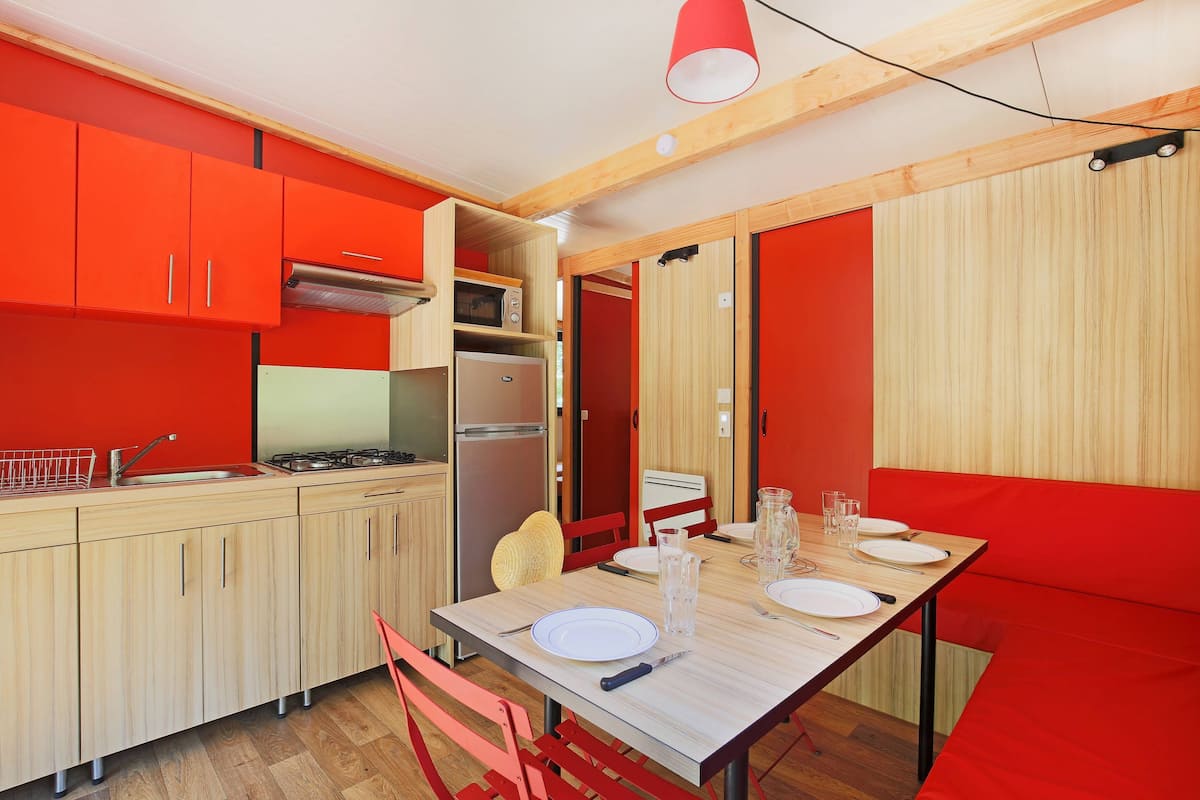 A compact kitchen with modern appliances, a dining area with a wooden table and red chairs, and a bright red accent wall.