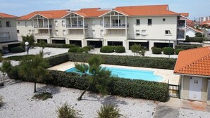 Ein mehrstöckiges Hotel mit Schwimmbad, umgeben von gepflegten Hecken und einer Kiesfläche.