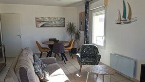 Ein Wohnzimmer mit einer Couch, einem Esstisch mit Stühlen, einem gemusterten Sessel, einem kleinen runden Tisch und einem Deckenventilator.