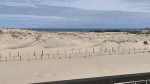 Ein Sandstrand mit einem Zaun und einem Leuchtturm im Hintergrund.