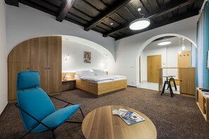 A modern bedroom with a bed, a blue chair, a round table, and wooden cabinets. - Prague Castle II (Prague)