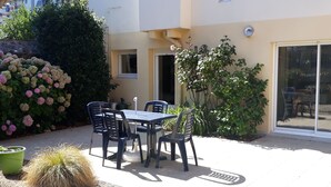 Un patio al aire libre con una mesa y sillas, rodeado de plantas en macetas y un cactus.