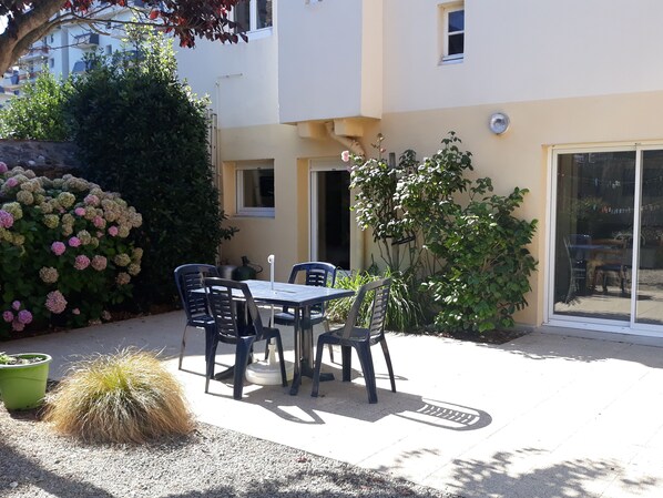 An outdoor patio with a table and chairs, surrounded by potted plants and a cactus.