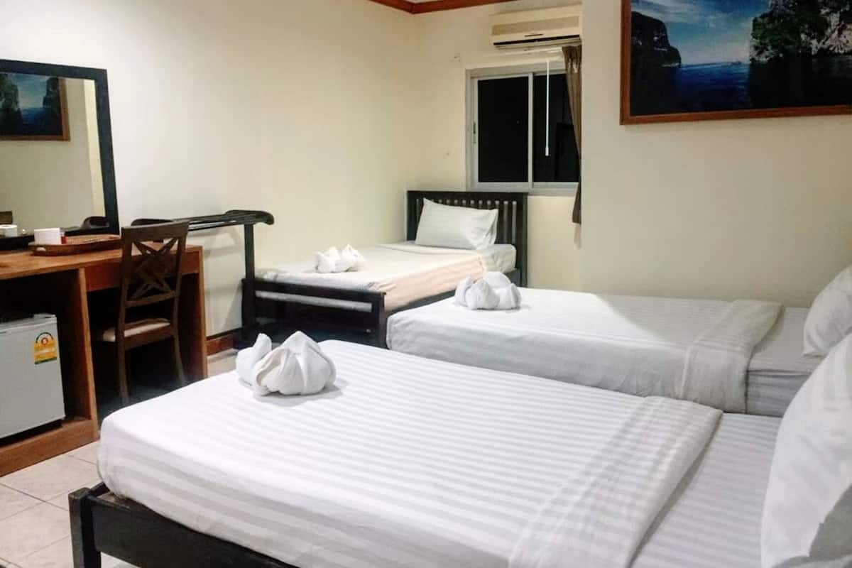 A hotel room with two single beds, a desk with a chair, a small refrigerator, and a window with curtains.