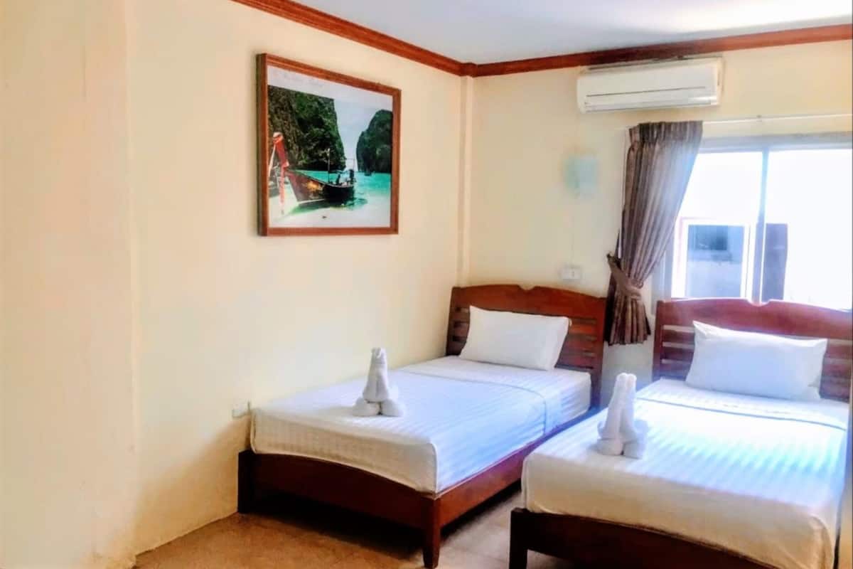 A hotel room with two beds, a painting of a boat on water, an air conditioning unit, and a window with curtains.