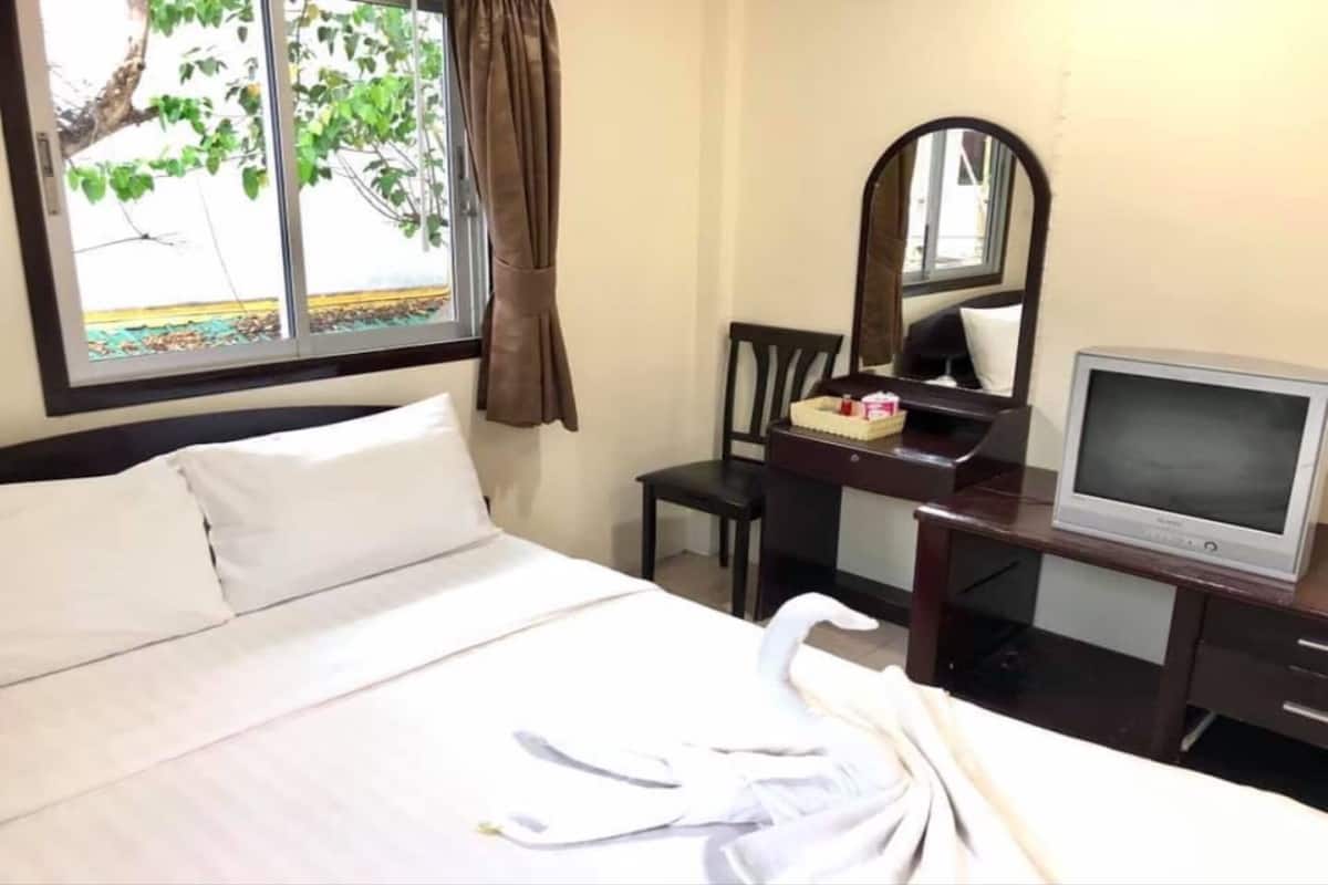 A hotel room with a bed, a desk with a television, a chair, and a mirror.