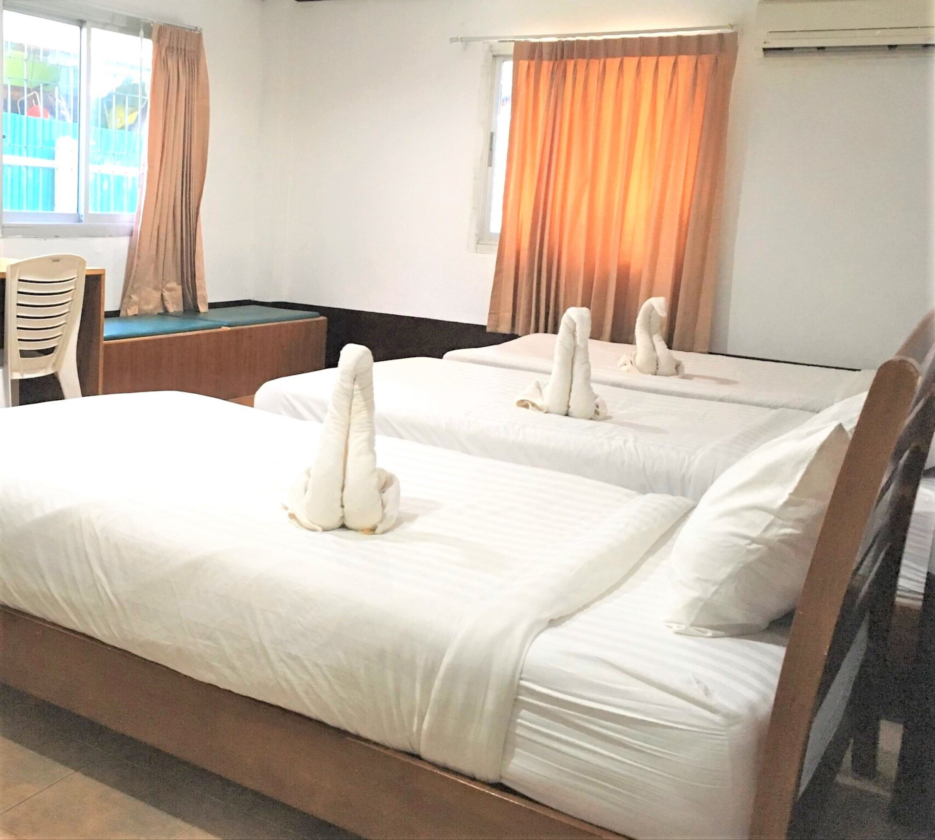 A hotel room with two beds, each with a towel sculpture, a desk, a chair, and a window with curtains.