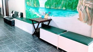 A seating area with a mural of a tropical landscape, a small table with a vase of flowers, and a sofa with a cushion. - Golden Bee PhiPhi Hostel (Ko Phi Phi)