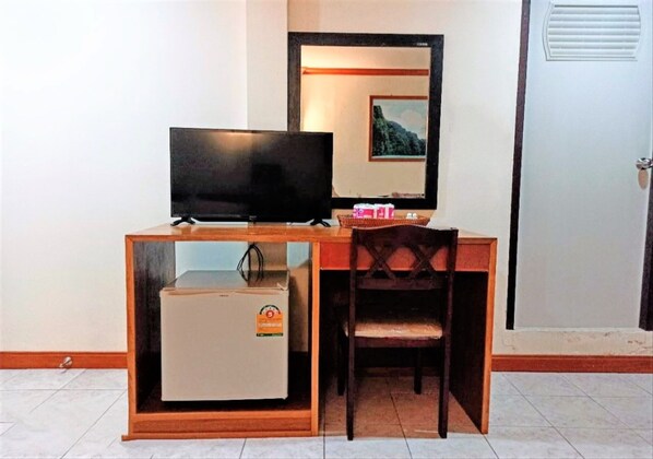A compact hotel room with a wooden desk, a television, a refrigerator, and a chair. - Golden Bee PhiPhi Hostel (Ko Phi Phi)