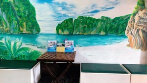 A mural of a tropical beach scene with a table displaying promotional materials. - Golden Bee PhiPhi Hostel (Ko Phi Phi)