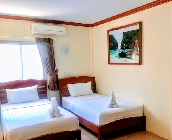 A hotel room with two single beds, a large window with curtains, an air conditioning unit, and a framed picture of a boat on water.