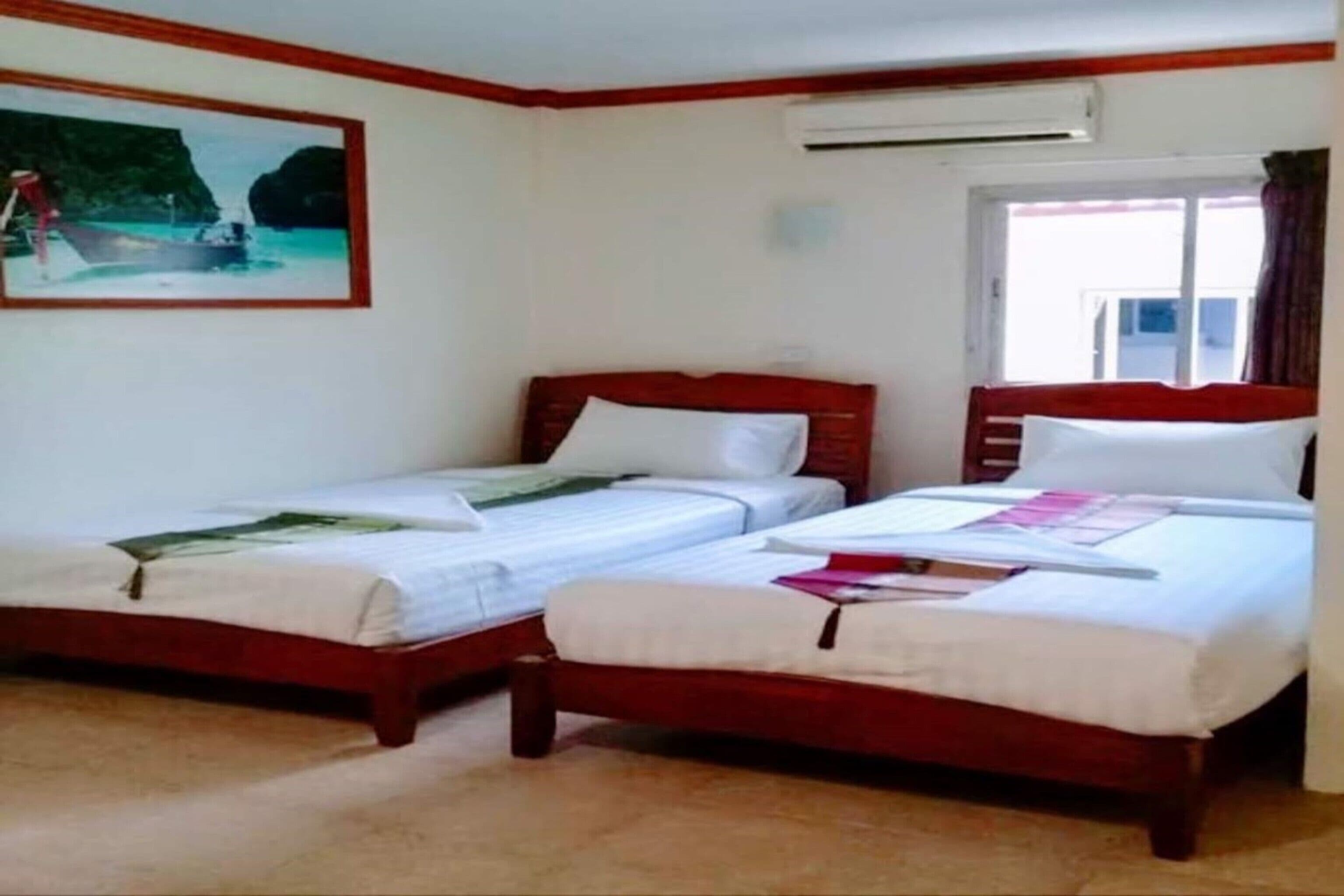 A room with two single beds, a painting of a coastal scene, an air conditioning unit, and a window with curtains.