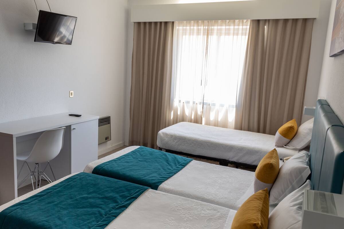 Hotellihuone, jossa on kaksi sänkyä, työpöytä, tuoli, televisio ja ikkuna, jossa on verhot.