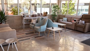 Una sala de estar moderna con un sofá, dos sillones, una mesa de centro y una mesita auxiliar. Hay un ventanal con vistas a la calle.
