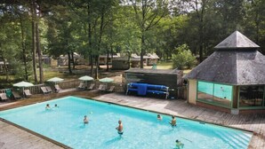 A swimming pool with people enjoying the water, surrounded by lounge chairs and umbrellas.