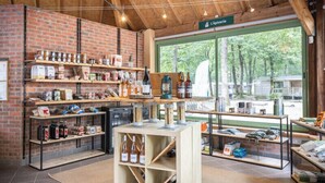 A rustic interior with wooden shelves displaying various products, a central table with bottles, and a large window offering a view of the outdoors.