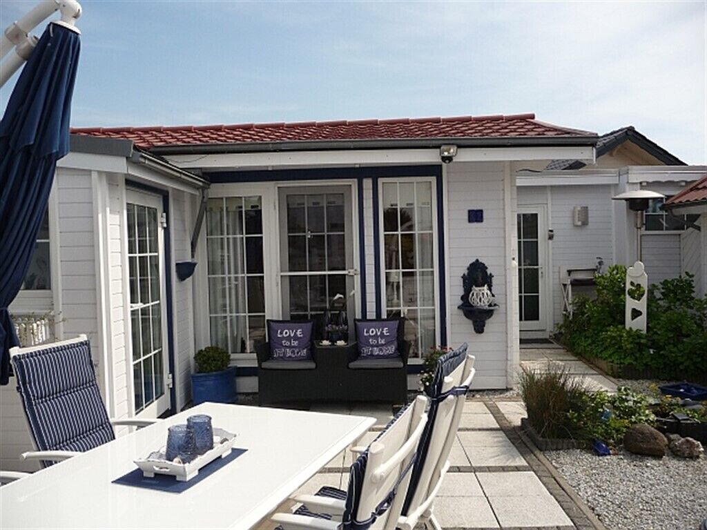 A white building with a red-tiled roof, a covered patio with a table and chairs, and a sign that reads "LOVE to be."