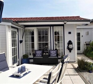 A white house with a red-tiled roof, a covered porch with two chairs, and a table with a tray. - Holiday house with a fantastic terrace (Wervershoof)