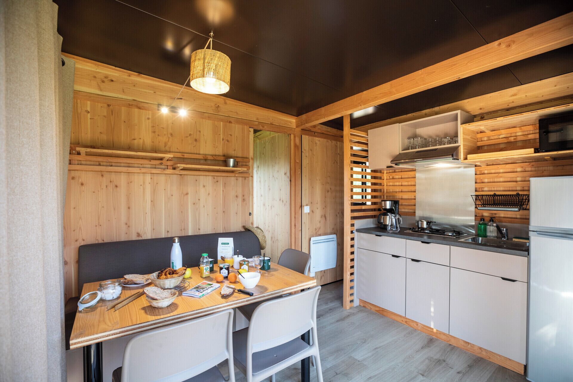 A compact kitchen with wooden walls, a dining table with breakfast items, and modern appliances.