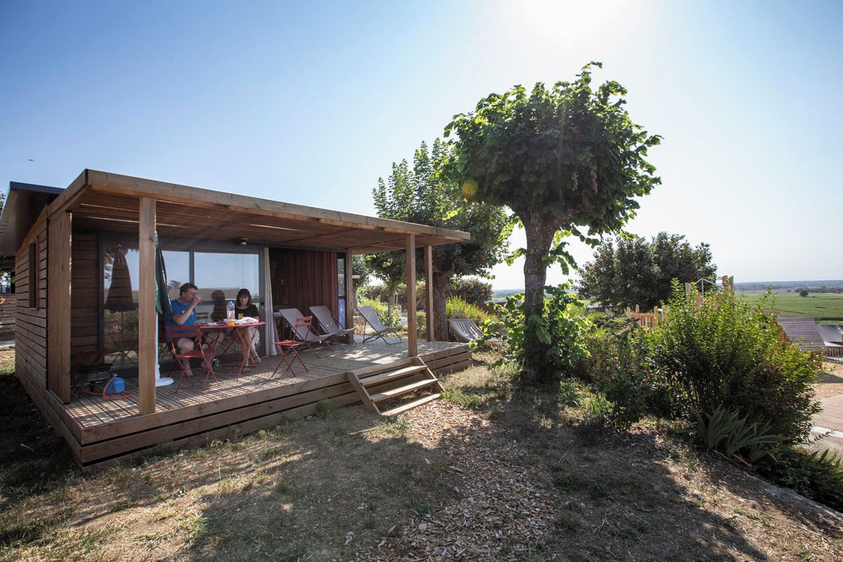 Eine Holzhütte mit einer Terrasse, Sitzgelegenheiten im Freien und Blick auf die Landschaft.
