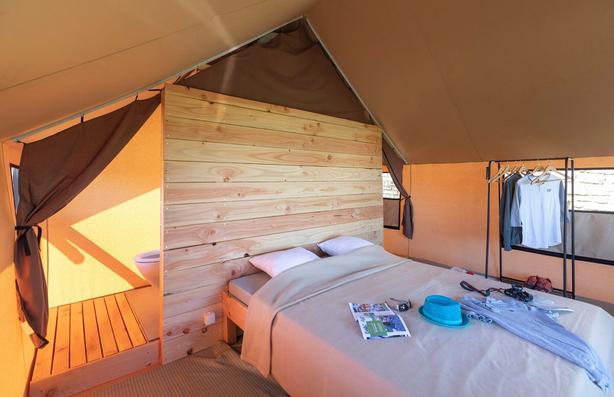 Une pièce aménagée avec une tente, un lit en bois, une petite table et une fenêtre.