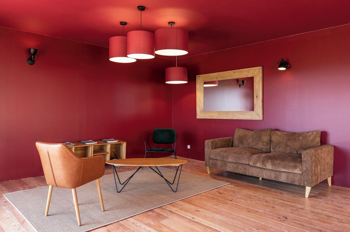A modern living room with a red wall, a brown sofa, a wooden coffee table, a brown chair, and a wooden floor.