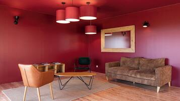 A modern living room with a red wall, a brown sofa, a wooden coffee table, a brown chair, and a wooden floor.